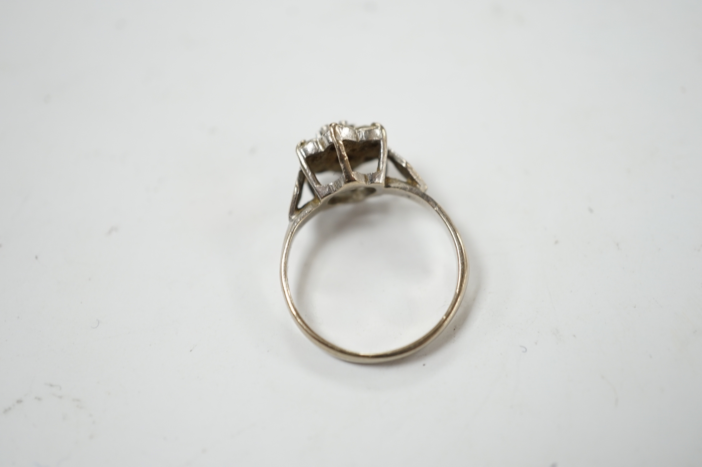 An 18ct white metal and seven stone diamond cluster set flower head ring (one stone missing), size K/L, gross weight 3.4 grams.